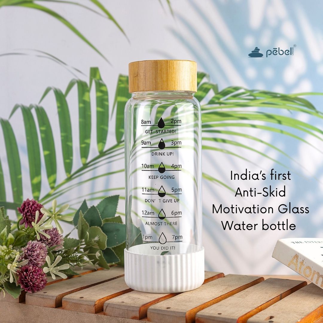 Glass water bottle with motivational markings on a wooden surface with greenery in the background