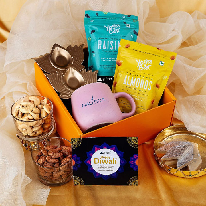 Gift basket with Nautica mug, 'Happy Diwali' card, and snacks on a yellow fabric background